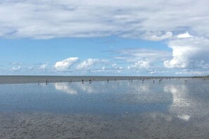 Ein Strand mit weitem Sandufer und einem klaren Himmel mit vereinzelten Wolken.
