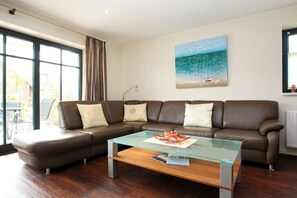 Ein Wohnzimmer mit einem Ecksofa, einem Glastisch und einem Gemälde mit Strandmotiv.