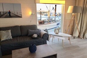 Un salon moderne avec un canapé, une table basse, une lampe et une vue sur un port de plaisance.