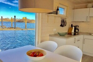 Eine moderne Küche mit weißen Schränken, einem Fenster mit Blick auf ein Gewässer und einem Tisch mit einer Obstschale.