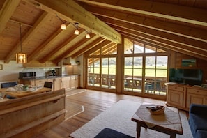 A spacious loft-style room with a high ceiling, wooden beams, a large sliding glass door to a deck, a dining area, and a television. - at the Martin Hirschbichler guesthouse (Inzell)