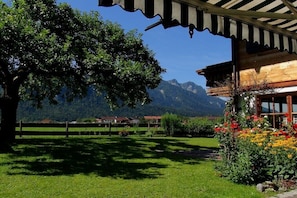 A wooden building with a sloped roof, surrounded by a well-maintained garden with colorful flowers and a large tree. - at the Martin Hirschbichler guesthouse (Inzell)