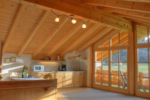 A wooden interior with a kitchen, dining area, and large windows. - at the Martin Hirschbichler guesthouse (Inzell)