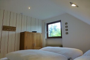 A bedroom with two beds, a wooden wardrobe, a window with a view of trees, and a sloped ceiling. - Holiday home in Piesport with barbecue (Piesport)