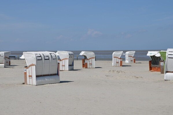Strandliegen auf einer Sandbucht, im Hintergrund das Meer.