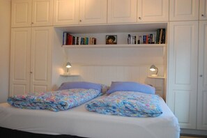 Ein Schlafzimmer mit einem Bett, zwei Nachttischlampen, einem Bücherregal und einem weißen Kleiderschrank.