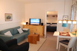 Ein Wohnzimmer mit einer Couch, einem Couchtisch, einem Fernseher und einem Essbereich mit Tisch und Stühlen.