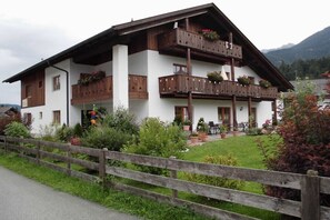 Ein zweistöckiges Gebäude mit hölzernen Balkonen, einer Veranda mit Sitzgelegenheiten und einem umlaufenden Garten.