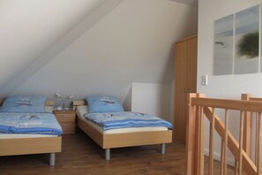 A bedroom with two beds, wooden flooring, a wooden wardrobe, and a staircase. - Holiday apartment with 2 bedrooms (Großenbrode)