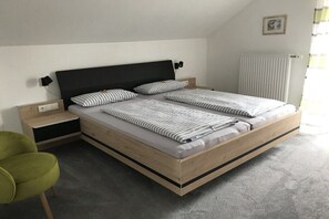 Ein modernes Schlafzimmer mit einem Bettgestell aus Holz, zwei Kissen, einem Nachttisch, einem grünen Sessel und einer Heizung.