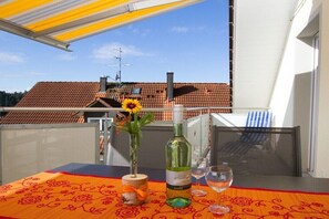 Ein Balkon mit Tisch für zwei Personen, einer Weinflasche und einem Blumenstrauß.