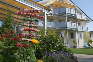 Ein mehrstöckiges Gebäude mit Balkonen, ein Garten mit Blumen und eine Schilder mit bunten Buchstaben.
