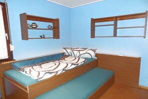 Ein kleines Zimmer mit einem Einzelbett, einer Bank und zwei Wandregalen mit Dekoration.