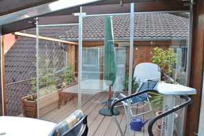 A covered patio with a table, chairs, a small garden, and a view of a house with a tiled roof. - Walnut tree in the holiday home by the plane (Haslach i.K.)