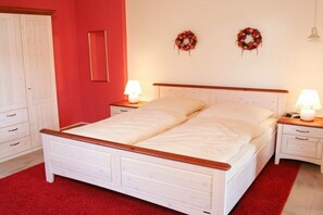 Ein Schlafzimmer mit einem weißen Bett, zwei Nachttischen mit Lampen, einem Kleiderschrank und zwei Wandkränzen.