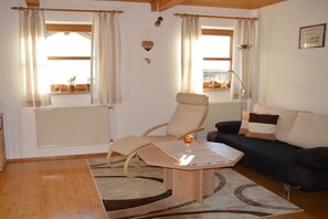 Ein Wohnzimmer mit einer Couch, einem Sessel, einem Couchtisch und einem Fenster mit Vorhängen.