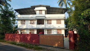 A two-story building with a flat roof, multiple windows, and a gated entrance. - SOUPARNIKA LAKEVIEW HOMESTAY LLP (Wayanad)