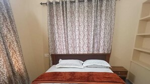 A bed with a white mattress and a brown headboard, a wooden nightstand, and a patterned curtain. - SOUPARNIKA LAKEVIEW HOMESTAY LLP (Wayanad)