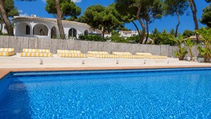Piscina com espreguiçadeiras, cerca de madeira e árvores ao fundo.