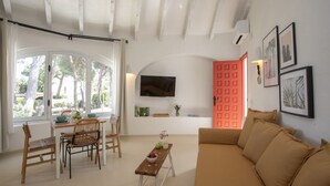 Uma sala de estar com sofá, mesa de jantar e cadeiras, televisão fixada na parede e uma porta vermelha.