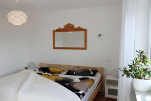 Ein Schlafzimmer mit einem Bett, einem hölzernen Kopfteil, einem Nachttisch, einem Spiegel und einer Zimmerpflanze.