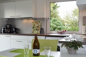A modern kitchen with white cabinets, a coffee machine, a bottle of wine, and a view of greenery outside. - Holiday apartment with 1 bedroom (Königstein im Taunus)