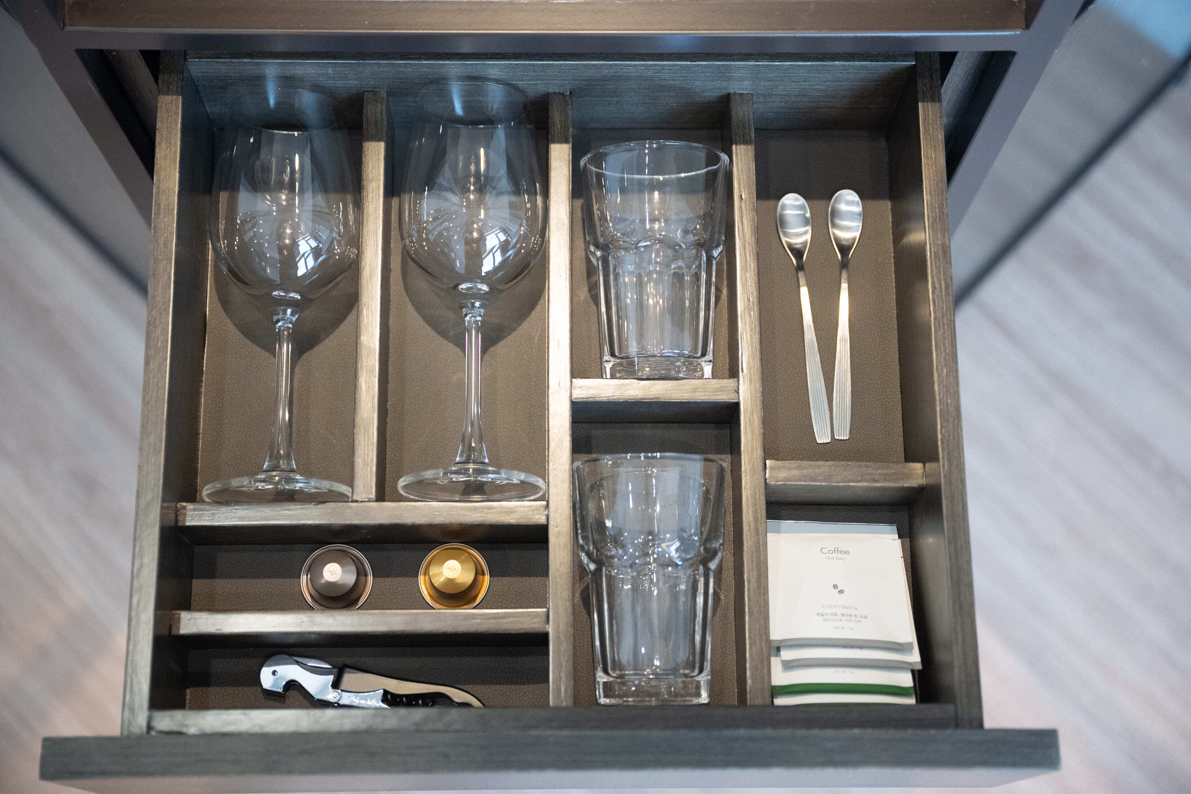 A drawer with wine glasses, a coffee cup, and a bottle opener.