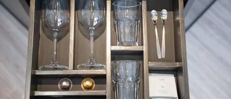 A drawer with wine glasses, a coffee cup, and a bottle opener.