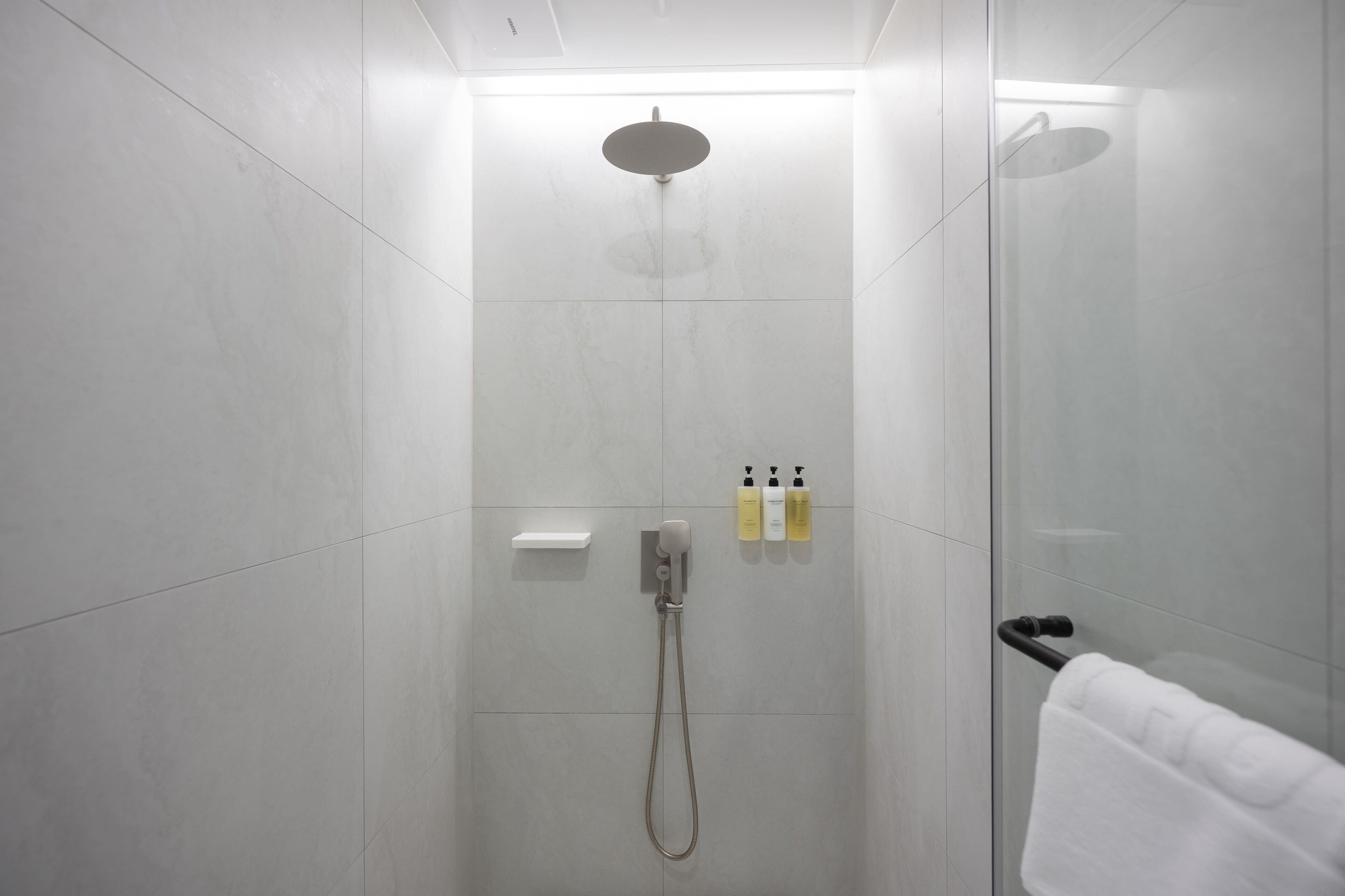 A modern shower with a handheld showerhead, a handheld shower attachment, and two bottles of shampoo and conditioner.