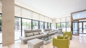 A spacious lobby with large windows, a sectional sofa, a glass coffee table, and a green armchair.