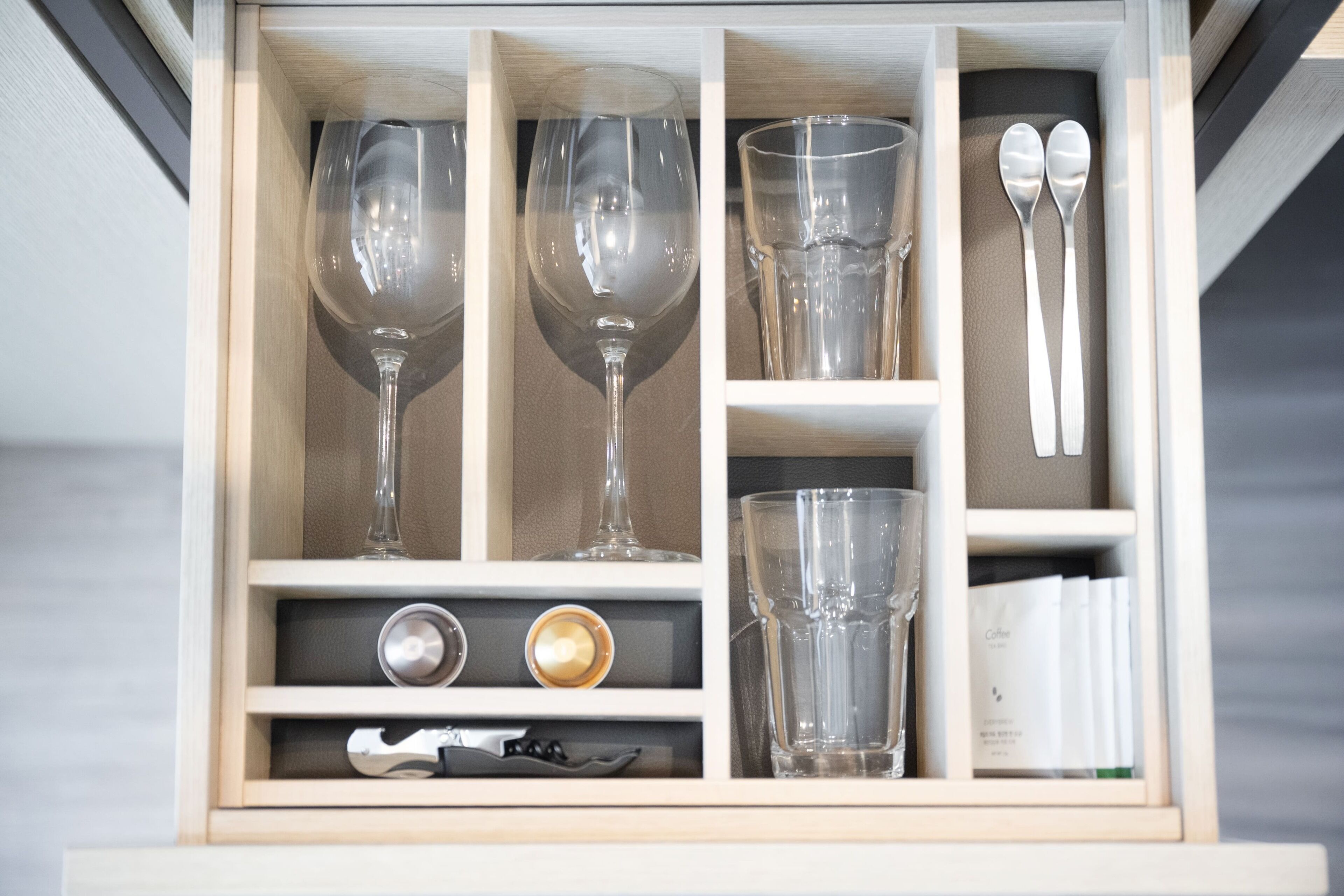 Un cajón con varios objetos de vidrio, incluyendo copas de vino, una taza de café y un juego de cucharas.