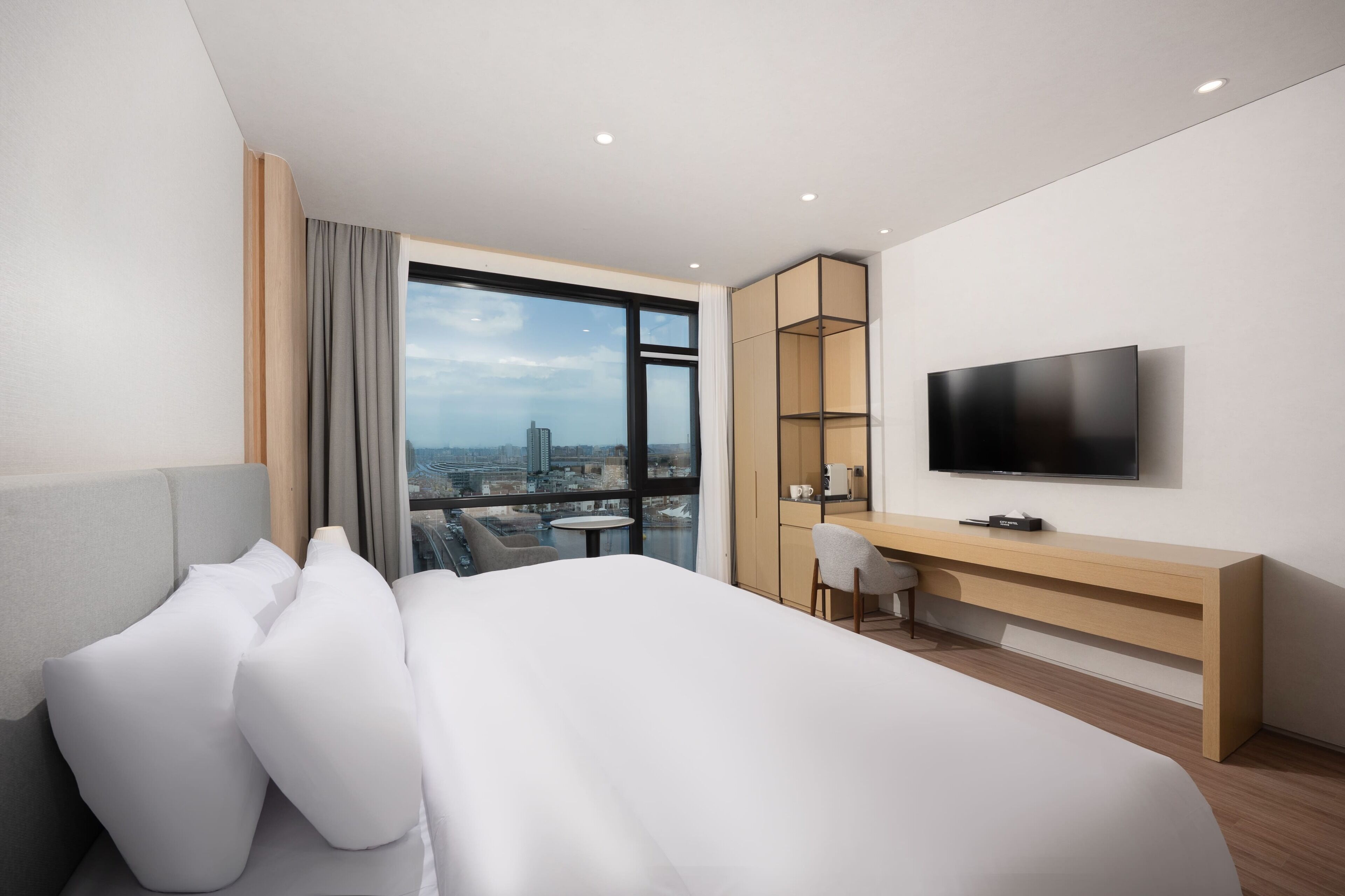 Et moderne hotelværelse med en stor seng, et fjernsyn, et skrivebord og udsigt over byen.