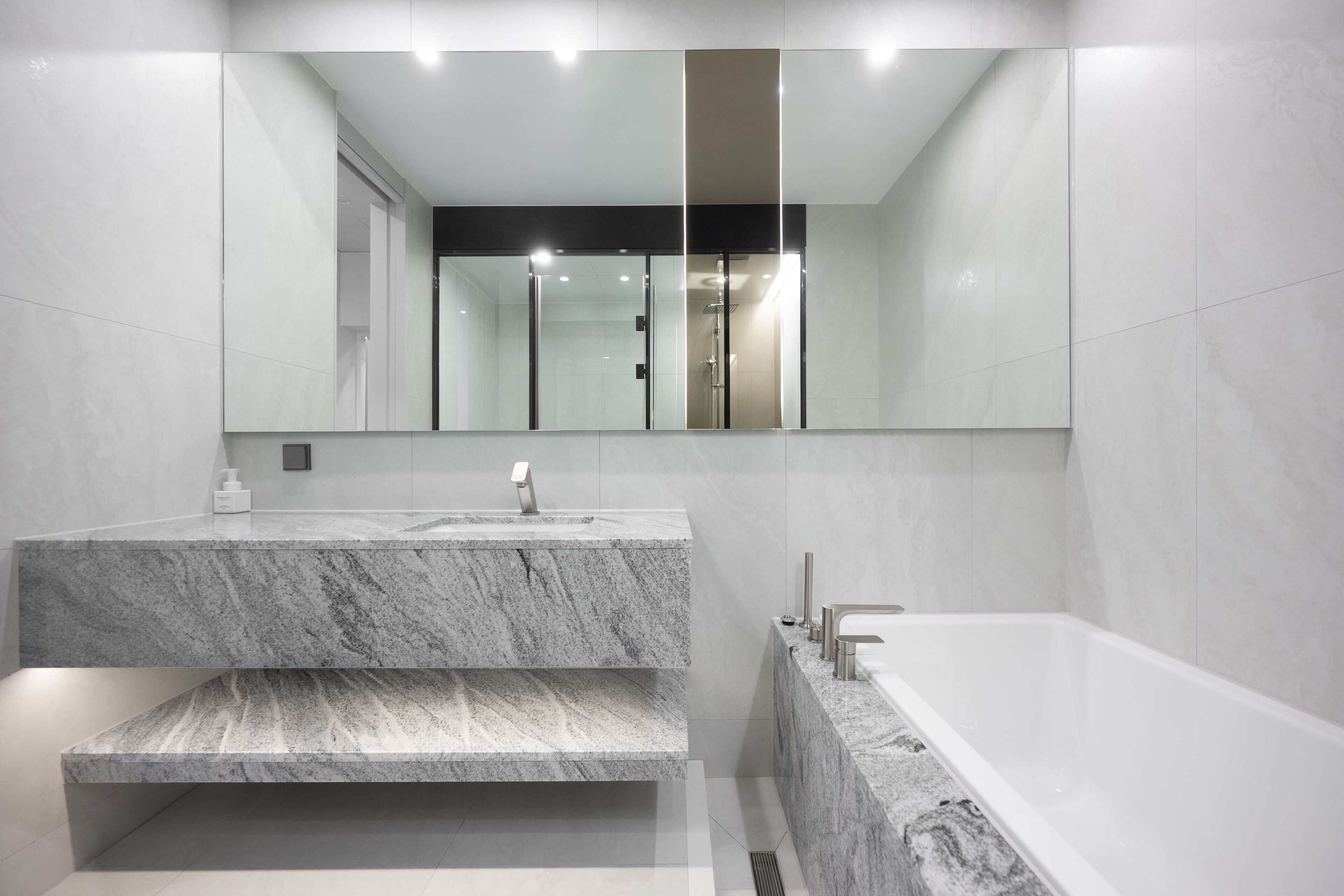 Une salle de bain moderne avec un meuble-lavabo en marbre, un grand miroir et une baignoire.