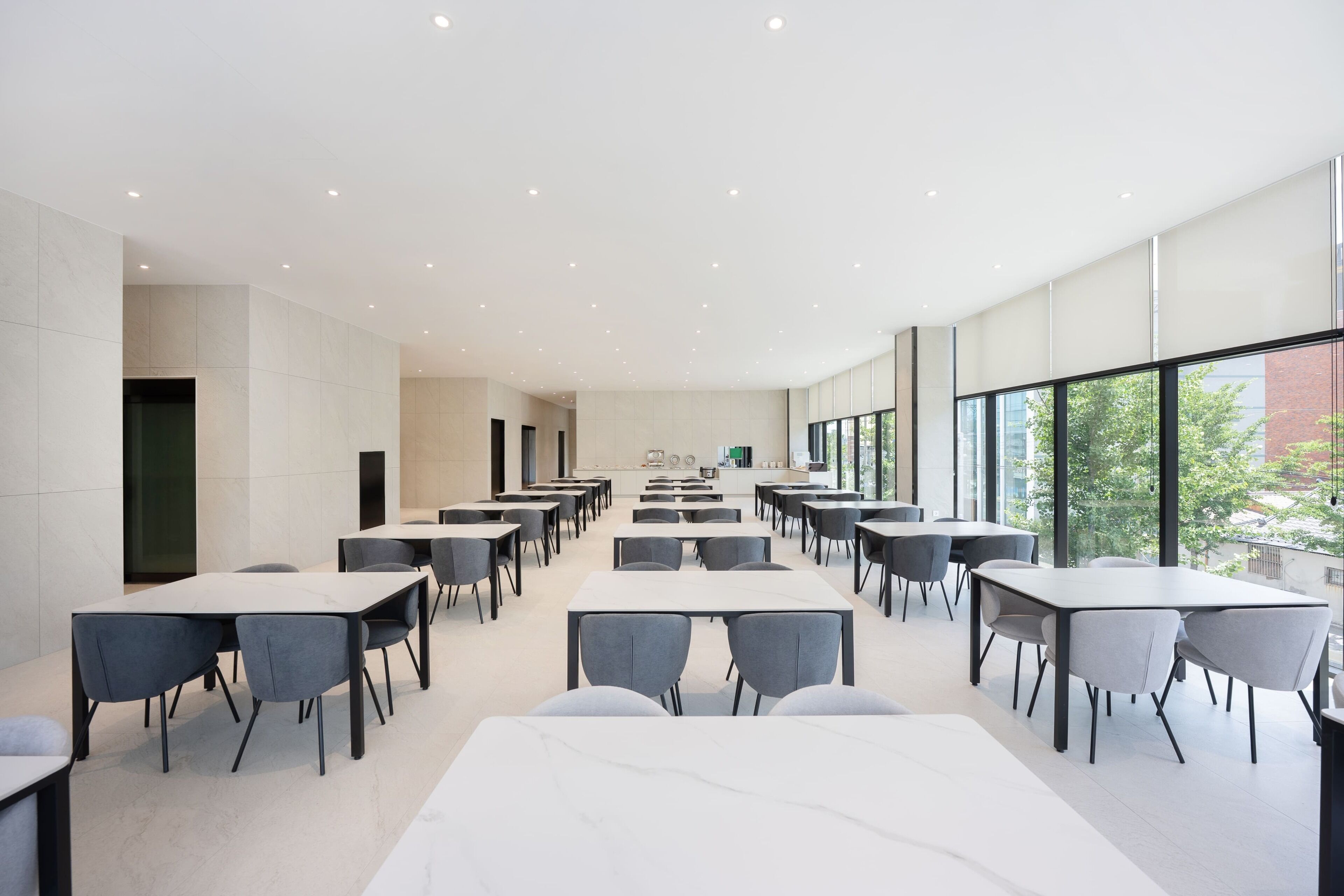 A spacious, modern dining area with multiple tables and chairs, large windows, and a clean, minimalist design.