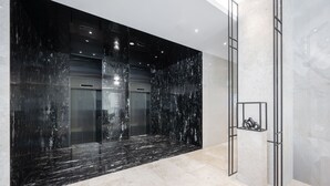 A modern lobby with a black marble wall, a glass elevator, and a metal column.