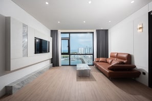 A modern living room with a flat-screen TV, a brown leather sofa, a marble accent wall, and a large window with a city view. - Pohang City Hotel (Pohang)