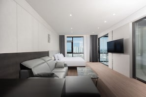 A modern hotel room with a bed, sofa, TV, and a city view. - Pohang City Hotel (Pohang)