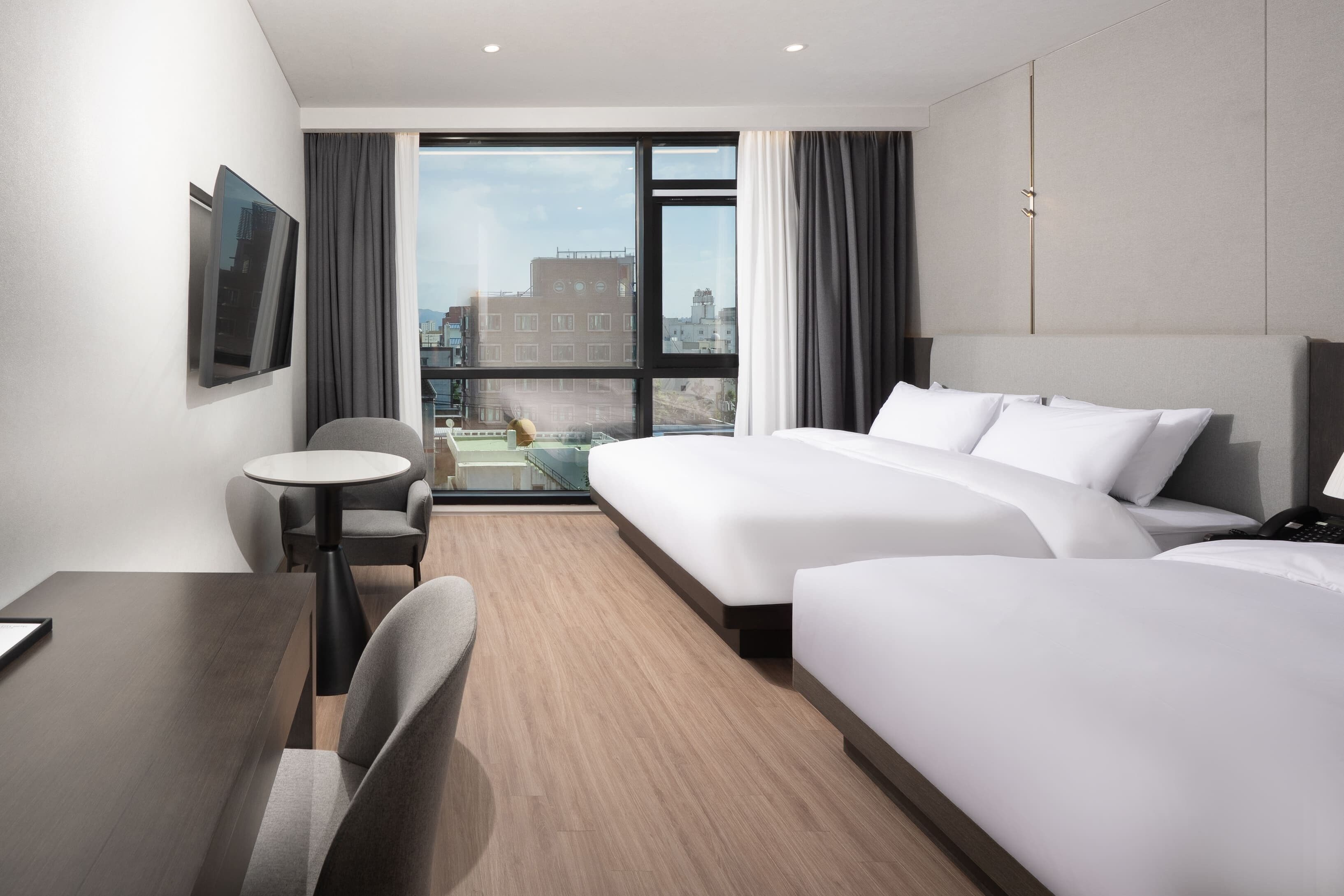 A hotel room with a bed, a desk, a chair, a TV, and a view of the city.