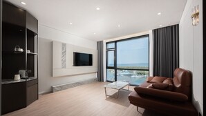 A modern living room with a sofa, a coffee table, a TV mounted on the wall, and a large window overlooking a marina.