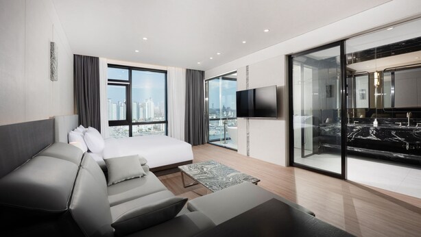 A modern hotel room with a bed, sofa, flat-screen TV, and a city view.