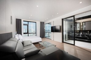 Una habitación de hotel moderna con cama, sofá, televisión de pantalla plana y vista a la ciudad.