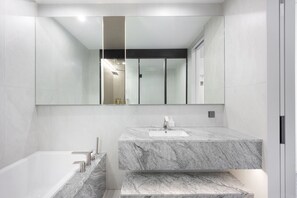 A modern bathroom with a marble sink, a large mirror, and a bathtub.