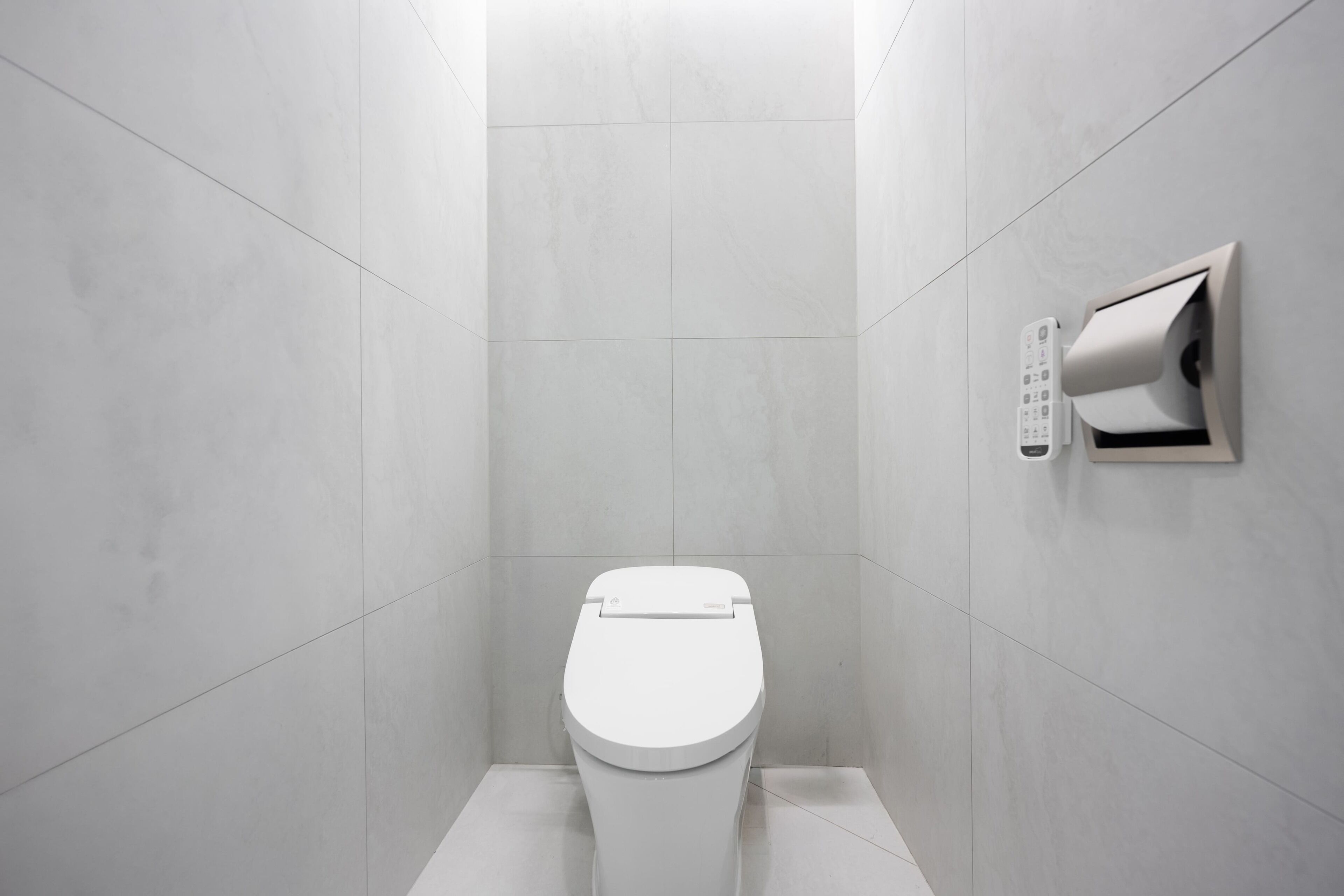 A modern bathroom with a toilet, a wall-mounted paper dispenser, and a clean, tiled floor.