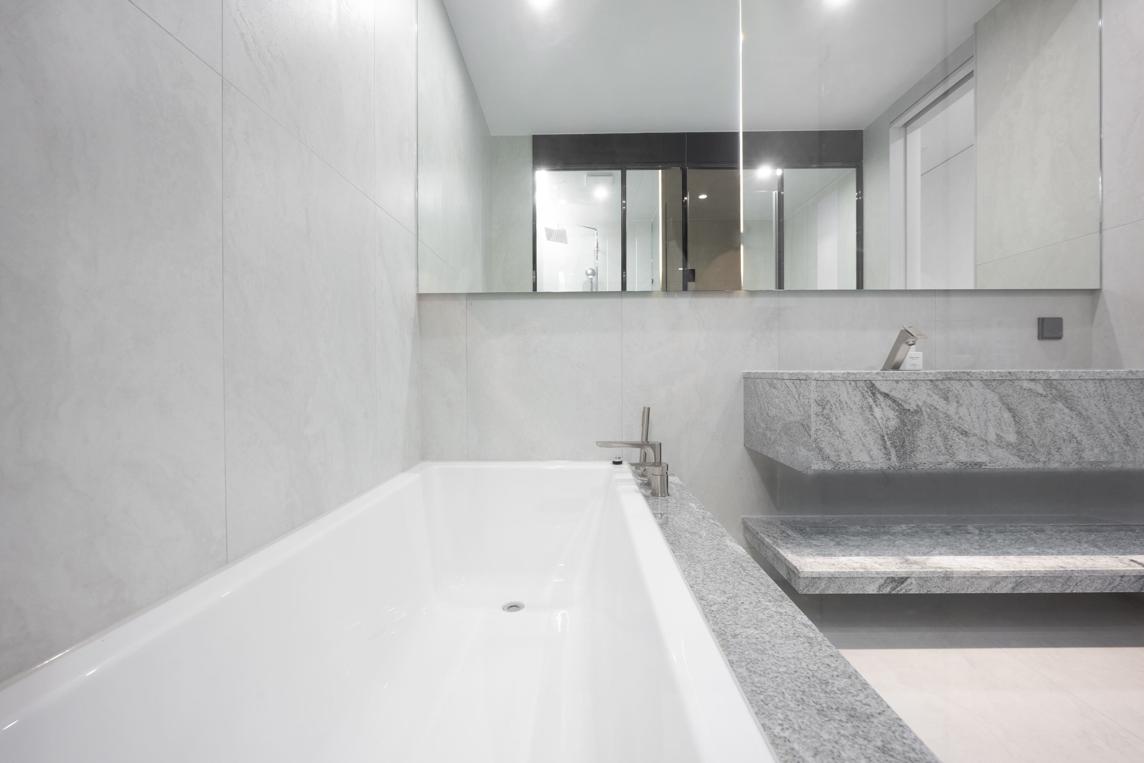 A modern bathroom with a large bathtub, a marble countertop, and a mirror above the sink.
