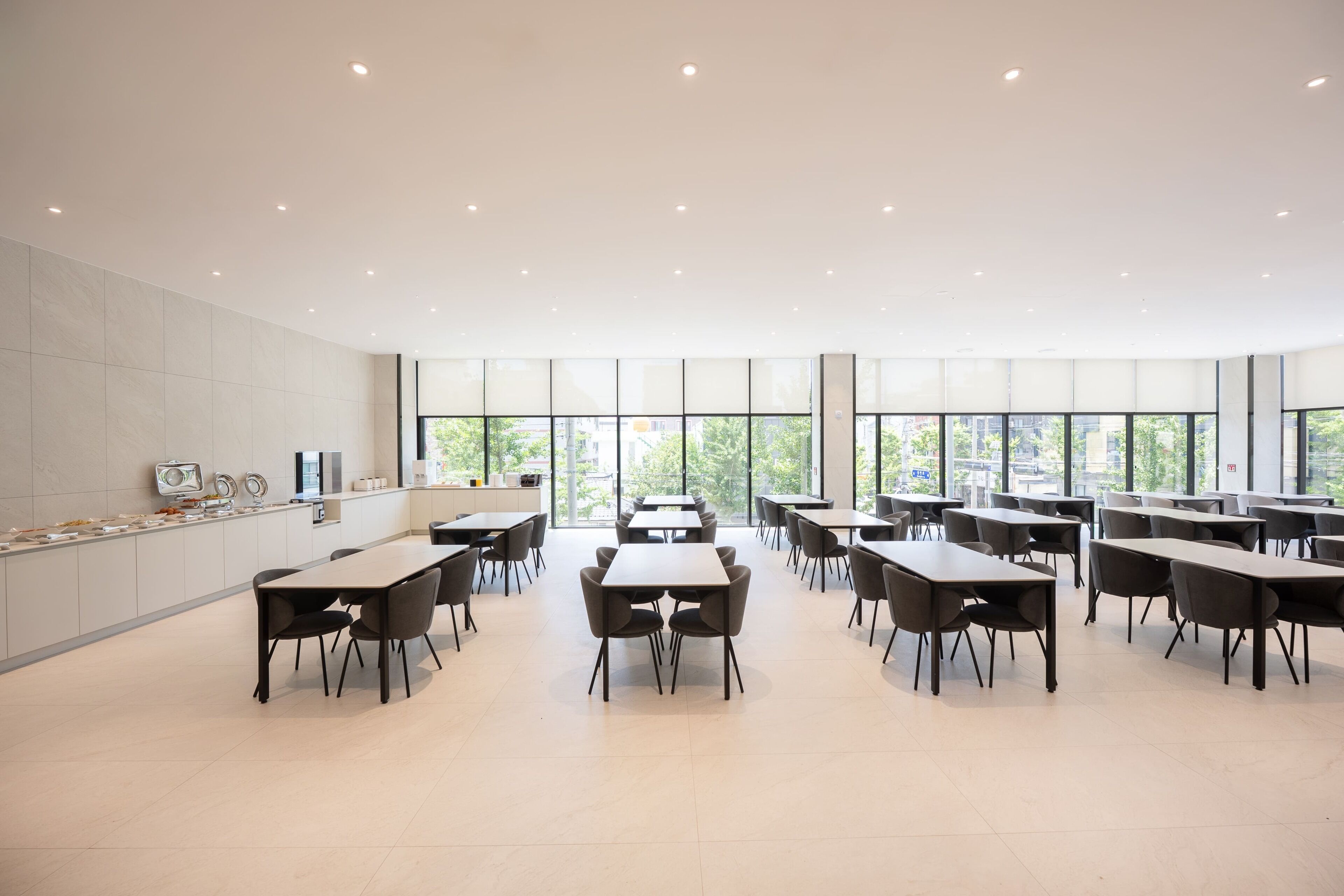 A modern dining area with tables and chairs, large windows, and a clean, minimalist design.