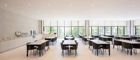 A modern dining area with tables and chairs, large windows, and a clean, minimalist design.