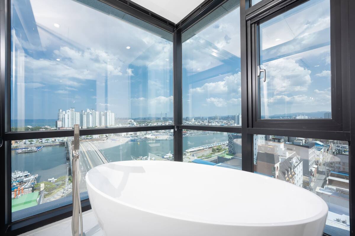 Un baño moderno con una bañera grande, ventanas amplias y vistas a un paisaje urbano.