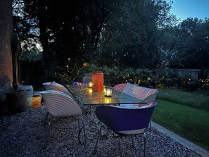 Ein Außenbereich mit Tisch aus Glas, Metallstühlen und dekorativen Laternen.