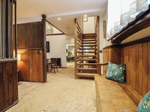 A wooden staircase leading to an upper floor, a herringbone-patterned floor, and a green floral pillow on a wooden bench.