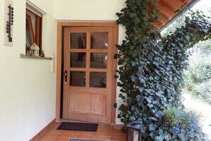 Eine Holztür mit Glasfenster, ein kleines Fenster mit einer Zierde und eine mit Efeu bewachsene Wand.